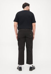 Black t-shirt with short sleeves, paired with dark brown cargo pants featuring side pockets, and black shoes with white socks visible.