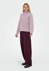 Pull en maille violet clair avec un col montant, des côtes texturées et des manches longues, associé à un pantalon bordeaux ample et des chaussures noires.