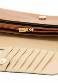 Portefeuille texturé marron avec une fermeture éclair dorée, comportant une étiquette "GUESS" ; l'intérieur comprend des emplacements pour cartes et un revêtement beige.