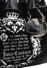 Zwarte fluwelen handtas met witte geborduurde tekst en ontwerpen, zilveren hardware en een zwarte leren hartvormige label eraan bevestigd.