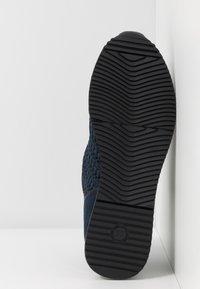 Marineblaue Sneaker mit einem strukturierten Obermaterial aus Stoff und einer schwarzen Gummisohle. Die Sohle hat ein wellenförmiges Profilmuster für besseren Halt. Größenlabel sichtbar.
