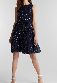 Mörkblå ärmlös klänning med vita prickar, insvängd midja med bälte, svängd kjol och mjukt, lätt tyg.