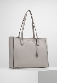 Borsa tote in pelle grigia con doppio manico, design strutturato, leggera brillantezza e un charm appeso a forma geometrica. Texture liscia e accenti lucidi.