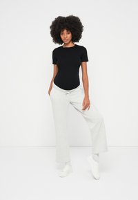Black short-sleeve bodysuit and light grey wide-leg sweatpants, paired with white sneakers, on a model against a plain background.