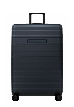 Black hard-shell suitcase with horizontal grooves, retractable handle, and four wheels for easy mobility. Includes a side luggage tag slot.
