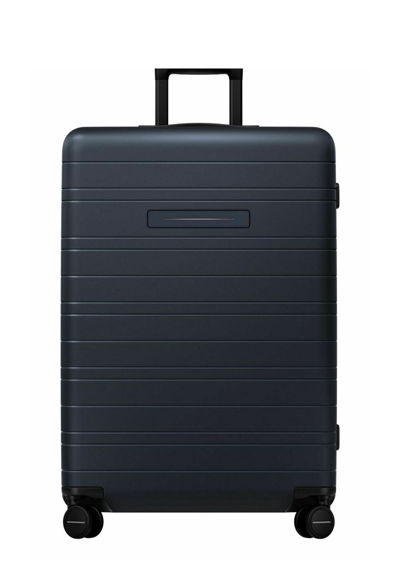 Valise rigide noire avec des rainures horizontales, poignée rétractable et quatre roues pour une mobilité facile. Comprend un emplacement pour une étiquette de bagage sur le côté.