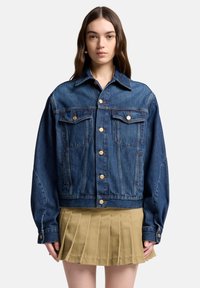 Kurtka dżinsowa o luźnym kroju, w ciemnoniebieskim kolorze, zapinana na guziki, z dwoma kieszeniami na piersi i szpiczastym kołnierzem. Charakteryzuje się widocznymi przeszyciami.