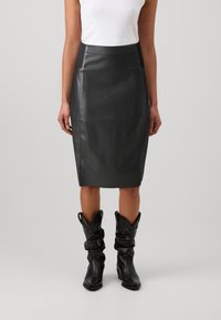 Svart läder kjol i blyertsstil med en slät yta, med hög midja och sömmar på sidan. Matchas med höga, svarta, viktiga cowboystövlar.