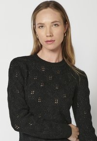 Czarny sweter z dzianiny z teksturowanym wzorem i otwartymi detalami. Długie rękawy i okrągły dekolt podkreślają jego design.