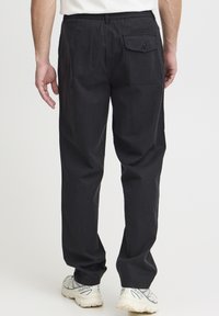 Pantalones negros de corte holgado con cintura elástica, bolsillos laterales y traseros, y una tela de algodón suave. Llevados con zapatillas de color claro.