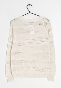 Pull en maille beige clair avec des motifs ajourés, une coupe décontractée et des poignets côtelés. Suspendu sur un cintre en métal noir sur fond blanc.
