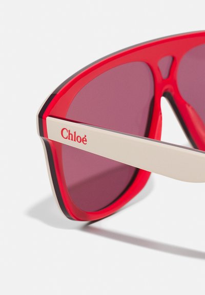 Punased prillid julge ja kaarekujundusega. Omavad tumedaid lense, kontrastset valget tempelosa ning külje peal on brändinimi "Chloé" punases kirjas.