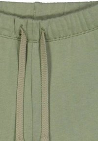 Primo piano di pantaloni tuta verde chiaro, dotati di vita con cordino, texture morbida e fascia elastica a costine con cordini beige a contrasto.