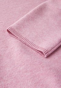 Zbliżenie na miękką różową dzianinę, ukazujące złożony rękaw z detalem ściągacza.