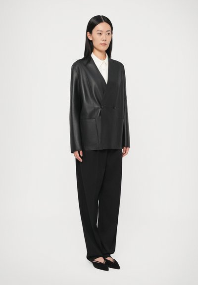 Melnas ādas divrindu žakete ar garām piedurknēm, priekšējām kabatām un brīvu piegriezumu, kombinēta ar melnām augsta vidukļa biksēm un melnām dzīvoklajām kurpēm.