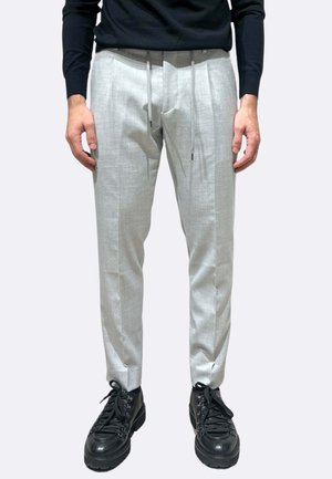 Pantaloni su misura di colore grigio chiaro con finitura testurizzata, vita con coulisse e tasche laterali, abbinati a scarpe nere con lacci.