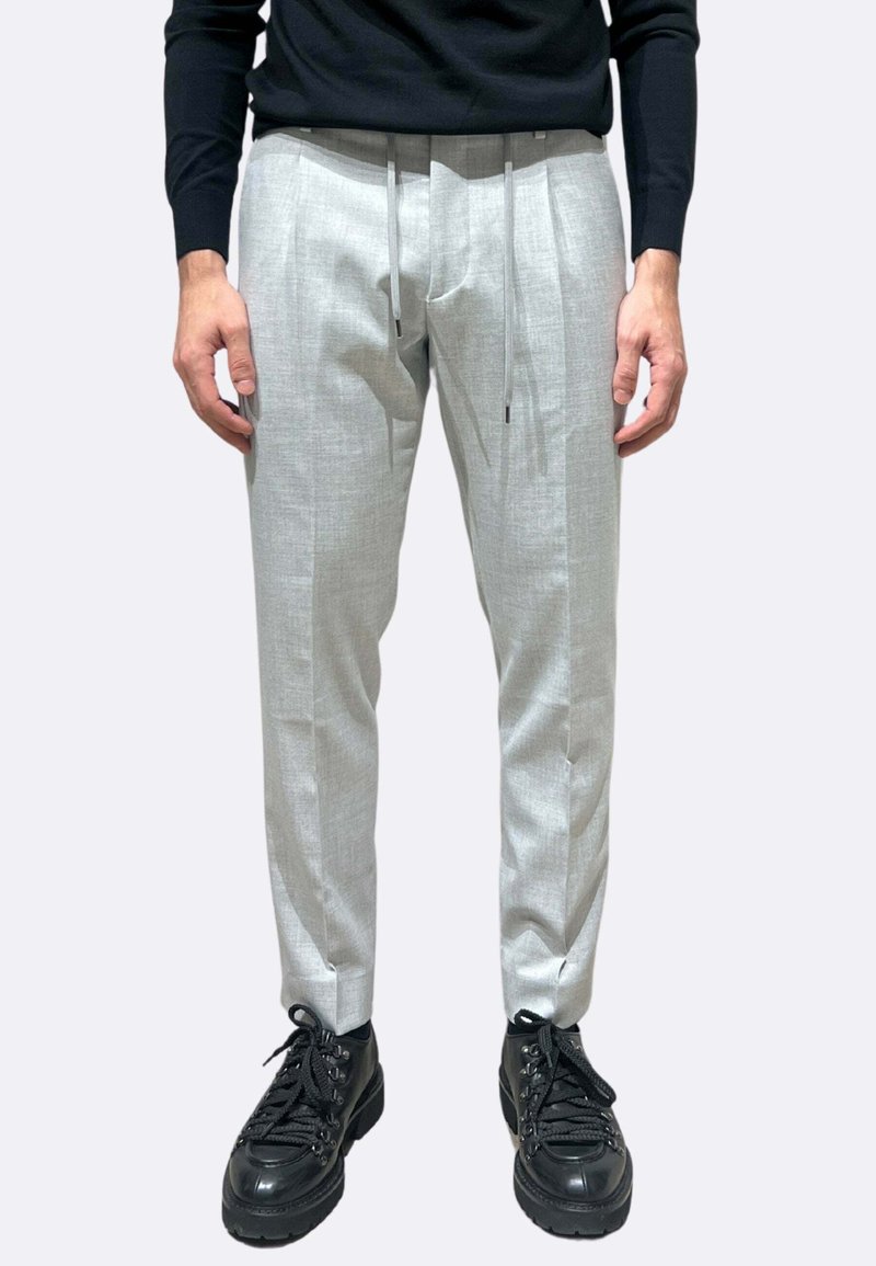 Pantaloni su misura di colore grigio chiaro con finitura testurizzata, vita con coulisse e tasche laterali, abbinati a scarpe nere con lacci.