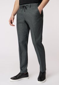 Pantaloni grigi texturizzati con vita regolabile tramite cordoncino, motivo sottile, tasche laterali e vestibilità su misura, abbinati a sneakers nere.