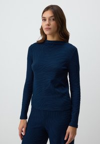 Top a maniche lunghe blu navy con un design a motivo onda testurizzato. Il tessuto sembra morbido e leggermente aderente, con scollo a giro.