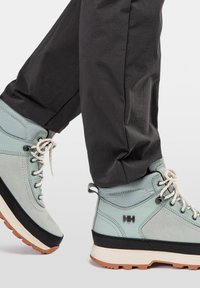 Botas de senderismo azul claro con detalles grises y suelas negras, que presentan costuras y cordones, combinadas con pantalones oscuros.