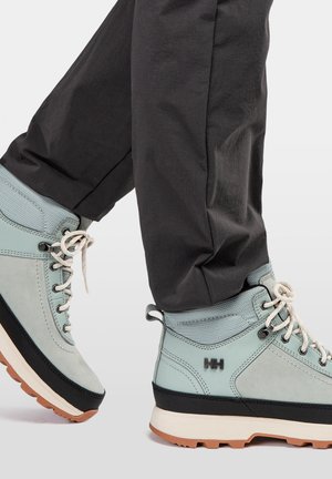 Lichtblauwe wandelschoenen met grijze accenten en zwarte zolen, voorzien van stiksels en veters, gecombineerd met een donkere broek.