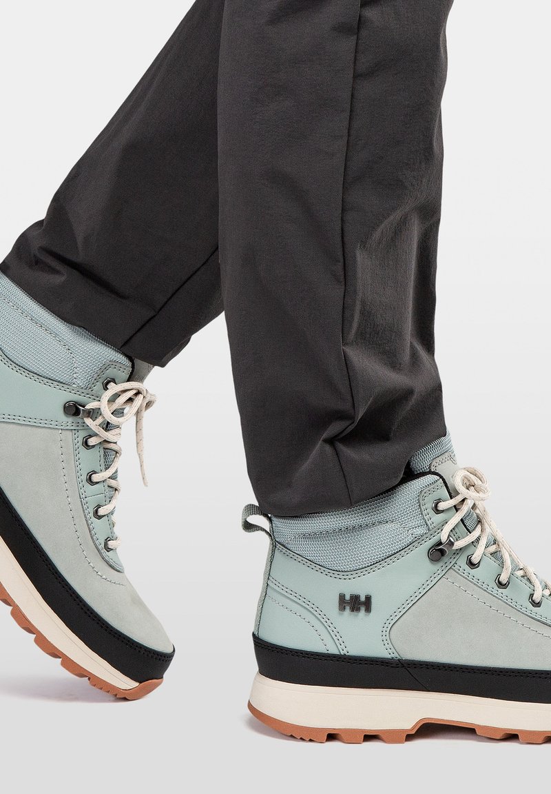 Botas de senderismo azul claro con detalles grises y suelas negras, que presentan costuras y cordones, combinadas con pantalones oscuros.