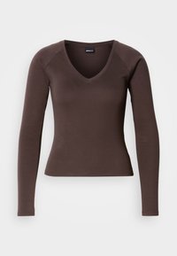 Καφέ μακρυμάνικο τοπ με V λαιμόκοψη και εφαρμοστή σιλουέτα, κατασκευασμένο από απαλό ελαστικό ύφασμα, με ραγκλάν μανίκια και καθαρές ραφές.