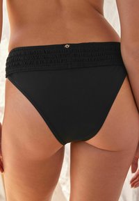 Fekete bikini alsó ráncolt derékkal, sima textúrával és minimális fedettségi dizájnnal. Arany logó akcentussal a hátsó részen.