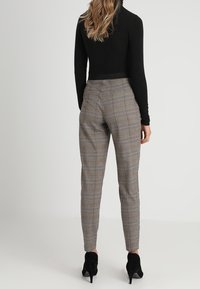 Szare spodnie w kratę z brązowymi akcentami, dopasowany krój, zwężane nogawki i kieszenie boczne, w zestawieniu z dopasowaną czarną bluzką i wysokimi obcasami.