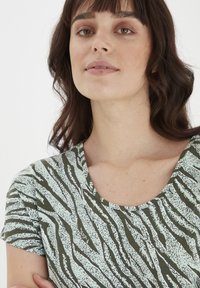 Zaļš un gaiši zils īsām piedurknēm t-krekls ar teksturētu zebras rakstu, kam ir apaļa kakla izgriezums un mīksts audums.