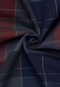 Dettaglio ravvicinato di un tessuto attorcigliato con un motivo a quadretti blu navy, verde scuro e bordeaux, caratterizzato da sottili linee gialle e bianche.