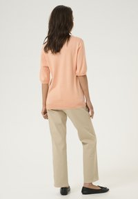 Maglione pesca con maniche a sbuffo corte, abbinato a pantaloni dritti beige e ballerine nere. Texture liscia, vestibilità comoda.