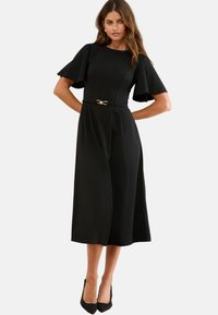 Rochie neagră cu mâneci scurte tip fluture, talie bine definită evidențiată de o curea cu ton auriu și fustă de lungime până la genunchi în stil A-line.