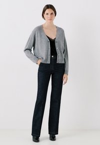 Cardigan grigio in lana con scollo a V, chiusura con bottoni e maniche lunghe, abbinato a jeans a zampa d'elefante in denim scuro e stivaletti neri alla caviglia.