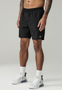 Black swim shorts with an elastic waistband and side pockets, made of lightweight material, paired with white athletic shoes and socks.