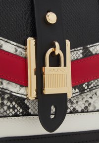 Czarna torebka z teksturowanej skóry z zapięciem na złotą kłódkę. Akcenty obejmują czerwone i białe paski oraz wzór węża.