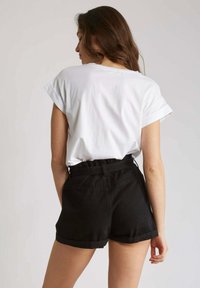 T-shirt blanc à manches courtes avec des revers, associé à un short en denim noir taille haute avec un ourlet replié et des poches.