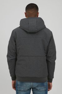 Gray puffer jacket with a hood, featuring a textured finish, horizontal stitching details, and a ribbed hem and cuffs. Worn over blue jeans.