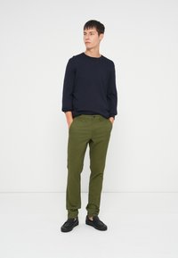 Suéter azul marinho de gola redonda combinado com calças chino verdes-oliva e sapatos pretos de deslizar. Design simples com um corte descontraído e texturas suaves.