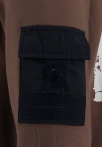 Prenda marrón de manga larga con un bolsillo de parche azul oscuro con cierre a presión, tela texturizada y detalles de rayas horizontales.