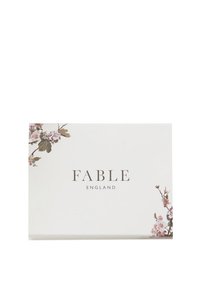 Belo pravokotno pakiranje z rožnimi poudarki v roza in bež barvi. Na sprednji strani sta elegantno natisnjena besedi "FABLE" in "ENGLAND" v sivi pisavi.