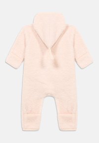 Combinaison en polaire rose avec capuche, texture douce, comprenant un accent pompon au dos et des poignets côtelés aux manches et aux jambes.