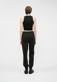 Čierny skrátený tielko skombinované s voľnými čiernymi teplákmi s elastickým pásom a zbernými manžetami, z pohľadu zozadu.