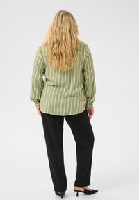 Ljusgrön randig blus med långa ärmar, kombinerad med svarta byxor och spetsiga svarta klackar. Blusen har vertikala krämfärgade ränder.