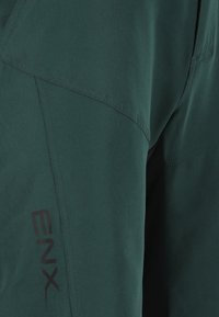 Mörkgrönt tyg med en slät struktur och synliga sömmar. En svart logotyp "ENX" är tryckt nära botten, vilket betonar varumärkets identitet.