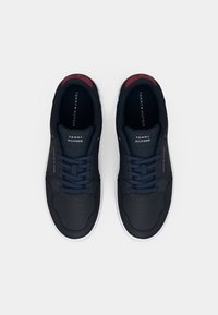 Une paire de baskets bleu marine Tommy Hilfiger avec des semelles blanches, des lacets bleu marine et des accents rouges, vue de dessus sur un fond blanc.