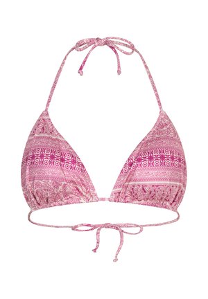 Woman with long hair wearing a pink patterned tie-side bikini standing near wooden door and green plant indoors.