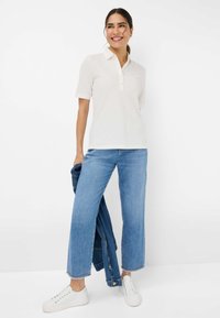 Hvid polo skjorte med korte ærmer og en tre-knap lukning, parret med lyseblå brede jeans og hvide sneakers.