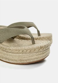 Espadrilové sandály s olivově zelenými textilními pásky, středovou částí z juty, texturovanou béžovou stélkou a plochou hnědou gumovou podrážkou.