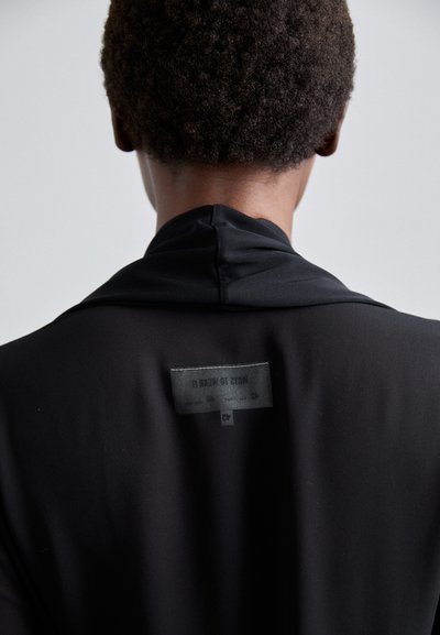 Black garment featuring a smooth, matte texture with a collar. A label on the back reads "MAYBE TO WEAR IT."